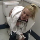 An attractive blonde girl is video-recorded by her friend as she pees into a toilet while standing and accidentally gets some pee on herself and fingers while trying to wipe.